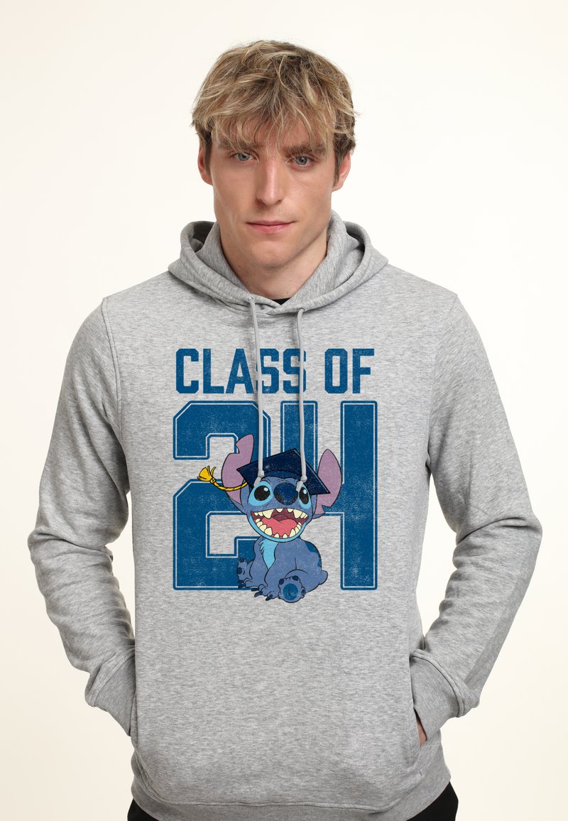 Młody mężczyzna w szarej bluzie z kapturem z napisem "CLASS OF 21" i kreskówkową niebieską postacią obcego w czapce absolwenta.