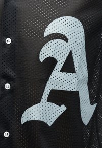 Μαύρο πλεκτό ύφασμα με λευκά κουμπιά και ένα μεγάλο λευκό στυλιζαρισμένο γράμμα "Α" τυπωμένο στο υλικό.