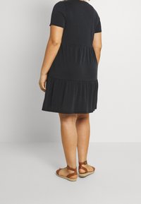 Robe noire à manches courtes avec un ourlet en couches, fabriquée en tissu doux. Assortie à des sandales à lanières marron avec une semelle en espadrille.