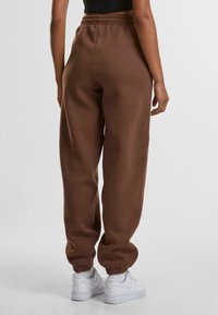 Bruine sweatpants met elastische tailleband en boorden, gemaakt van zachte stof, met een losse pasvorm en zijzakken. Gemaakt om te dragen met witte sneakers.