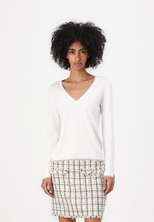 Maglione bianco a maniche lunghe con scollo a V e finitura testurizzata, abbinato a una gonna in tweed multicolore con dettagli di bottoni.