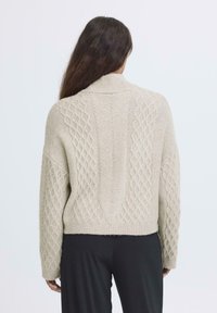 Maglione lavorato a maglia beige chiaro con colletto alto, caratterizzato da motivi a diamante testurizzati e una vestibilità leggermente cropped. Maglia morbida e spessa.