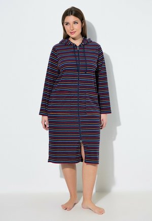 Frau steht barfuß und trägt ein knielanges, marineblaues Hoodie-Kleid mit Reißverschluss, mehrfarbigen horizontalen Streifen und Fronttaschen.