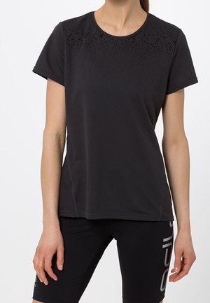 Femme portant un maillot de sport noir à manches courtes avec un motif sur le haut de la poitrine et un short de cyclisme noir avec du texte blanc sur la jambe gauche.