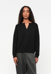 Zwarte sweatshirt met een V-hals, voorzien van textuurdetail bij de hals, lange mouwen en een getailleerde taille. Zacht materiaal en een relaxte pasvorm.