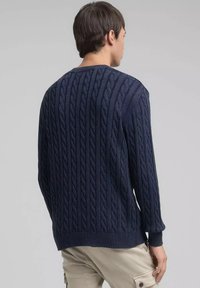 Marineblauwe kabelgebreide trui met lange mouwen en geribbelde zoom. Het gestructureerde patroon toont gedraaide kabels over de rug en mouwen.