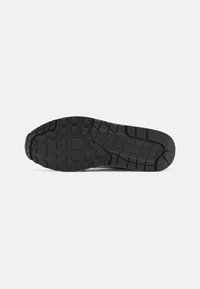 Black rubber shoe sole with a textured surface, featuring rectangular and circular patterns for traction and stability.