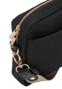 Sort stof tas med en gylden lynlås, prydet med et gyldent hardware-lås og en sort læderdetalje. Tekstureret overflade med en kontrastbund.