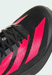 Czarny but sportowy z teksturowanym cholewką, z jaskraworóżowymi akcentami i czarnymi sznurówkami. Posiada gładką, zaokrągloną podeszwę dla lepszej przyczepności.