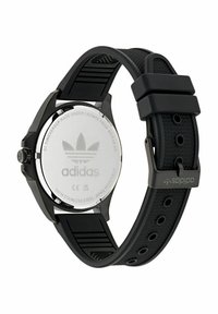 Montre de sport noire avec un bracelet en caoutchouc et un dos en acier inoxydable. Équipée d'un logo Adidas et d'un design de cadran circulaire.