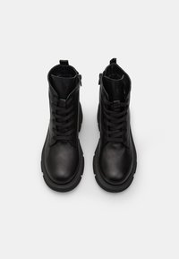 Botas de tobillo de cuero negro con cordones en la parte delantera, cremallera lateral, punta redonda, suela texturizada y acabado suave. Diseño simple y funcional.
