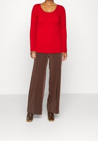 Rotes, geripptes Langarmshirt mit U-Boot-Ausschnitt, kombiniert mit braunen, weit geschnittenen Hosen und braunen Stiefeletten mit quadratischer Spitze.