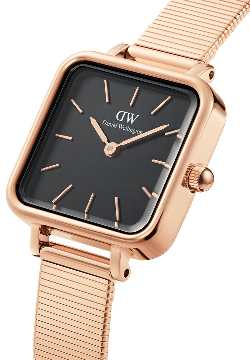 Kwadratowy zegarek na rękę z czarną tarczą, różowo-złotą metalową obudową i siateczkowym paskiem. Posiada smukłe wskaźniki godzinowe i koronkę z boku.