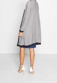Lång, lätt cardigan med ett geometriskt mönster i vitt och marin, med långa ärmar och en kontrasterande enfärgad marin kant.