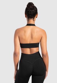 Zwarte sportbeha met een halternek ontwerp, een gladde textuur en een brede ondersteunende band, gecombineerd met hoge zwarte leggings.