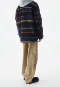 Camicia di flanella blu marino con righe orizzontali multicolori, abbinata a pantaloni cargo beige con tasche laterali e calzature nere.