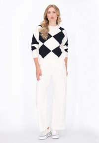 Gebreide trui in wit en marineblauw, met een argyle-patroon. Combinatie met witte wide-leg broek en witte sneakers.
