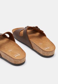 Smeđe kožne sandale s plutastom uloškom i crnom gumenom potplatom. Imaju dvije široke trake i teksturiranu unutrašnjost.