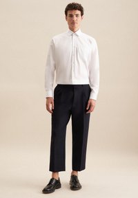 Biała koszula na guziki z kieszonką na piersi, zestawiona z granatowymi spodniami szerokimi w nogawkach i czarnymi sznurowanymi butami, na neutralnym tle.