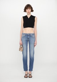 Black cropped tank top with scalloped edges, blue straight-leg jeans, and strappy black sandals. The model holds a small patterned bag.