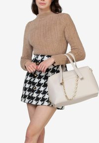 Beige fuzzy sweater, sort med houndstooth-mønster i sort og hvid, samt en cremefarvet håndtaske med en guldkædestrop.