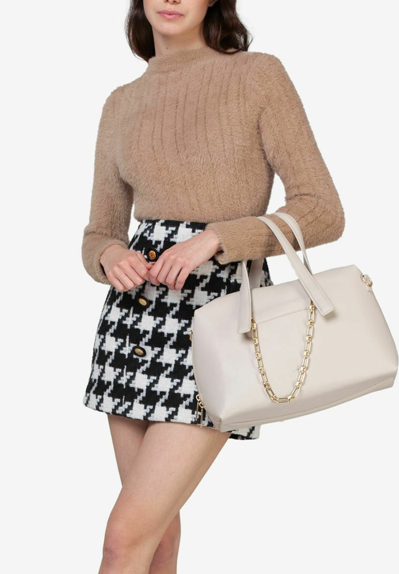 Beige fuzzy sweater, sort med houndstooth-mønster i sort og hvid, samt en cremefarvet håndtaske med en guldkædestrop.