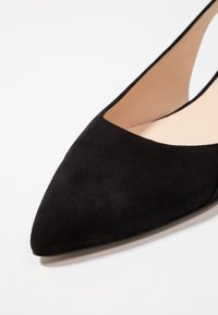 Zapato plano negro de ante con punta afilada y diseño recortado, que cuenta con un forro interior suave y una forma elegante y minimalista.
