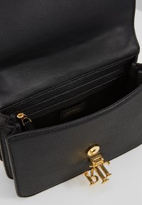 Czarna skórzana torebka o teksturowanym wykończeniu, z zapięciem z złotym okuciem i kieszenią wewnętrzną na zamek. Widoczna metka wewnątrz.