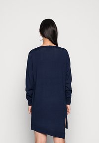 Robe en maille bleu marine avec manches longues, fentes latérales et coupe décontractée. Tissu texturé et ourlet côtelé apportent de la profondeur au design.