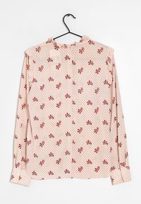 Skjorta med långa ärmar i ljusrosa tyg med röd blommönster och kontrasterande diamantskärning. Har en volangkrage och volang vid ärmsluten.