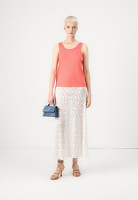 Korálový top bez rukávů, bílá krajková maxi sukně, světlomodrá kabelka a béžové sandály na popruzích. Hladká tkanina a vrstvené designové detaily.