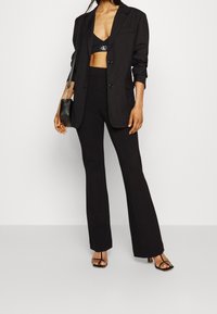 Musta räätälöity bleiseri mustan lyhyen paidan ja korkeavyötäröisten housujen päällä, yhdistettynä mustiin remmihenkisiin korkokenkiin ja pieneen mustaan käsilaukkuun.