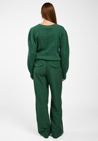 Groene fluffy trui met een brede halslijn, gecombineerd met hoge groene broek met een slanke witte zijstreep en achterzakken.