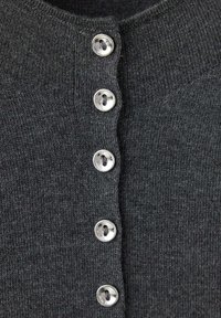 Gros plan d'un tissu tricoté gris foncé avec une rangée verticale de cinq boutons ronds argentés attachés au centre.