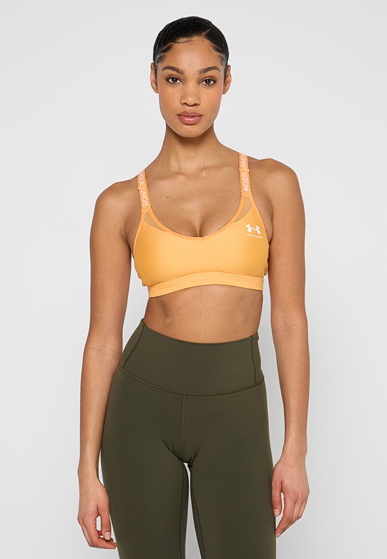 Pomarańczowy stanik sportowy z regulowanymi ramiączkami z logo "Under Armour". Gładki, elastyczny materiał; dekolt w kształcie litery U i design z plecami na ramiączka.