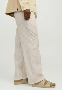 Pantalones de tejido texturizado color beige claro con un patrón vertical, corte recto y cinturilla elástica, combinados con sandalias beige de punta abierta.