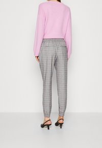 Pink knitted sweater with long sleeves paired with gray check-patterned trousers featuring an elastic waistband and cuffed ankles. Black low-heel sandals.