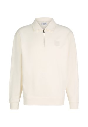 Langärmeliger, cremefarbener Pullover mit Kragen und halbem Reißverschluss, mit einem kleinen quadratischen Aufnäher auf der linken Brust.