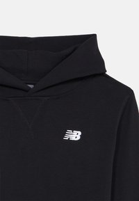 Melnā kapuce izgatavota no kokvilnas maisījuma, ar priekšu kangaroo kabatu, aukliņu kapuci un mazu baltu izšuvumu logotipu uz krūšu.