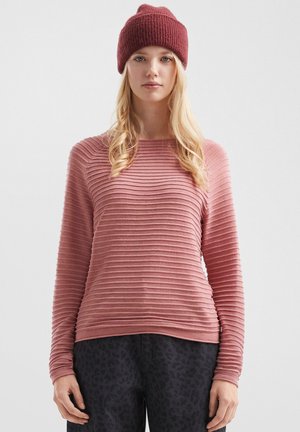 Stofroze geribde pullover met lange mouwen, zachte textuur, ronde hals, gecombineerd met donkere gemusterde broeken en een kastanjebruine gebreide muts.