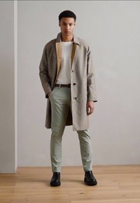 Lichtgewicht jas met een ruitpatroon en een beige binnenkant, gecombineerd met een wit T-shirt en mintgroene pantalons. Zwarte enkellaarsjes maken de outfit compleet.