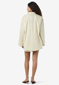 Kollaste ja siniste triipudega ülerohke särk, millel on pikad varrukad, nöppidega krae ja kõver hem, valmistatud kergest kangast.