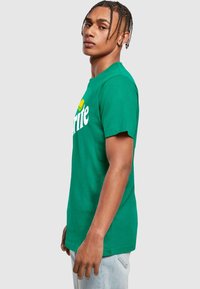 Grøn bomulds t-shirt med et hvidt "Sprite" logo, korte ærmer, rund hals og en afslappet pasform. Glat tekstur og rent design.