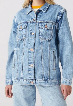 Veste en denim bleu clair effet acidulé avec fermeture par boutons, poches poitrine à rabat et poches latérales verticales portée avec un jean assorti.
