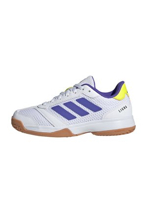 Zapatilla deportiva blanca con rayas moradas, lengüeta amarilla en el talón, suela de goma y logotipo "LIGRA" en el lateral.