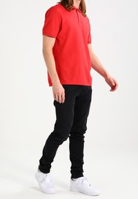 Červené polo tričko s límečkem, v kombinaci s černými úzkými kalhotami a bílými teniskami. Tričko má krátké rukávy a rovný střih.