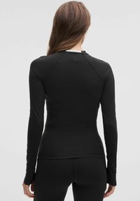 Must kere õhuke sportlik särk, millel on sile kangas ja keha lähedane lõige, raglansleeved ja seljaosas väike logo detail.