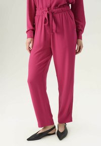 Pantaloni fucsia in tessuto intrecciato con fascia elastica in vita e laccio regolabile. Texture liscia, vestibilità dritta, con tasche laterali e gambe affusolate.