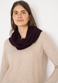 Écharpe infinity violette en tissu doux et texturé, drapée autour du cou. Portée avec un pull beige clair, mettant en avant un look décontracté.