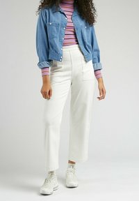 Jeansjacka i blått, vita byxor med vida ben och randig lila långärmad skjorta. Vita sneakers fulländar outfiten.